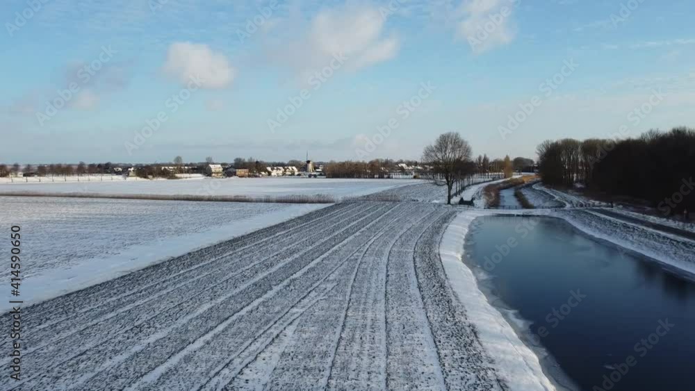 Drone flying over a dutch winter landscape. Frozen ditch, snow on the farmland. Dutch village in the distance. Drone flying over a dutch winter landscape. Frozen ditch, snow on the farmland. Dutch village in the distance.