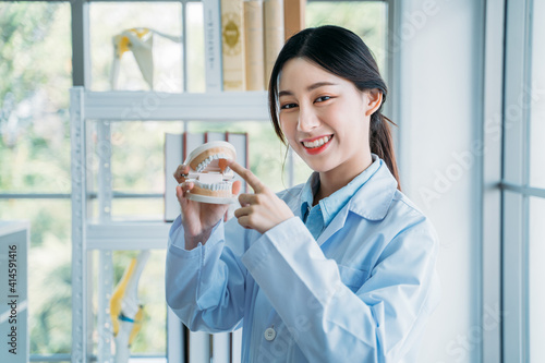 Portrait of happy and successful Asian dental doctor holding false teeth while explaining every teeth during online class for education on dentistry photo