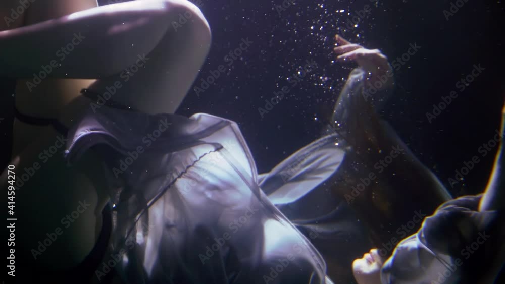 A beautiful woman is deep under the water on a dark background, floating creating a lot of bubbles. She's wearing beautiful underwear and fabric. A beautiful woman is deep under the water on a dark background, floating creating a lot of bubbles. She's wearing beautiful underwear and fabric.