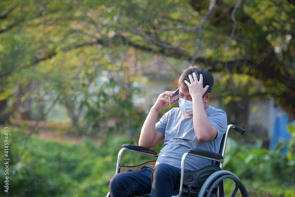 Young man suffering from depression sitting on a wheelchair talking on cell phone Green tree background Young man suffering from depression sitting on a wheelchair talking on cell phone Green tree background