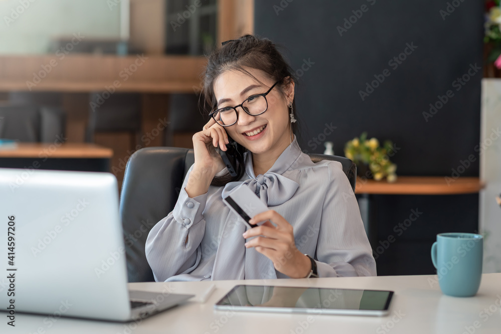 Beautiful smile Asian woman talking on mobile phone happy holding credit card at office.