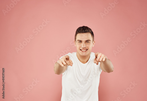 A man gestures with his hands in a white t-shirt emotions pink background