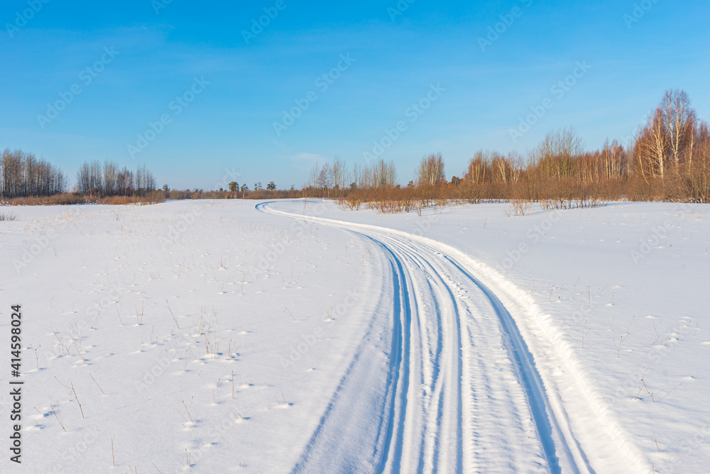 Snowmobile road on a snowy field. Winter landscape on a bright sunny day