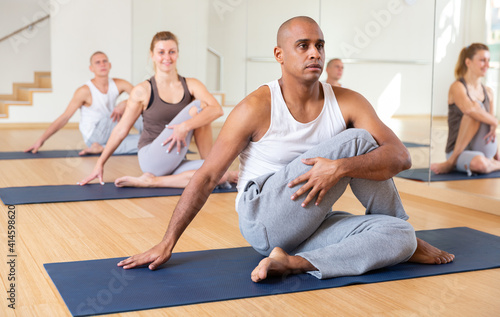 Young adult man exercising yoga with group of sporty people in studio