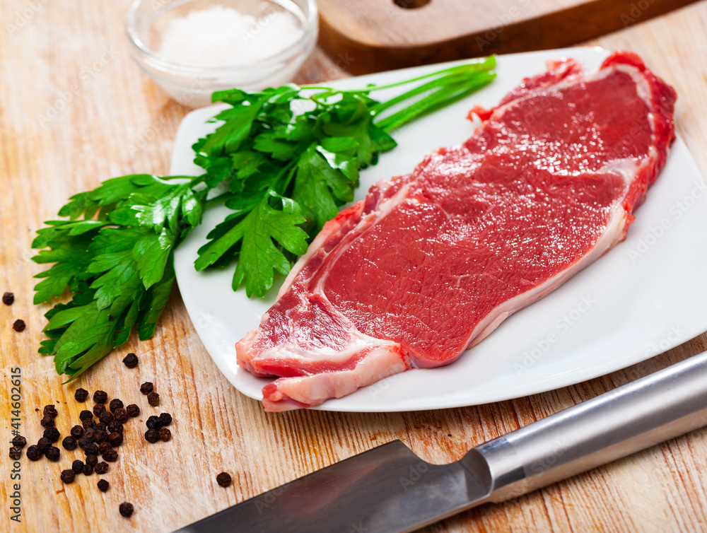 Fototapeta premium Piece of raw boneless beef on wooden background with seasonings and greens prepared for roasting