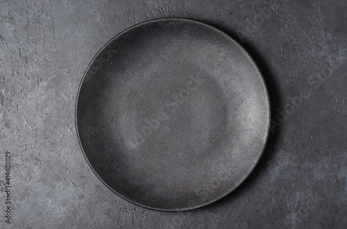 Dark grey textured concrete background for design with black food plate. Copy space