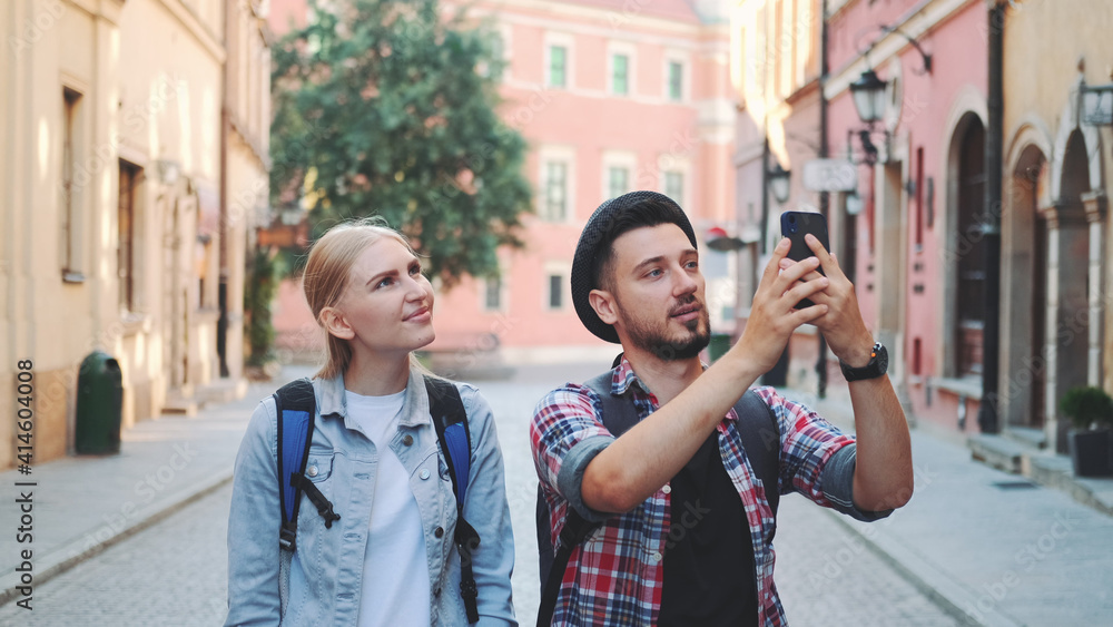 Young tourist couple walking on the street and making photos on smartphone. They admiring the beauty of surroundings.