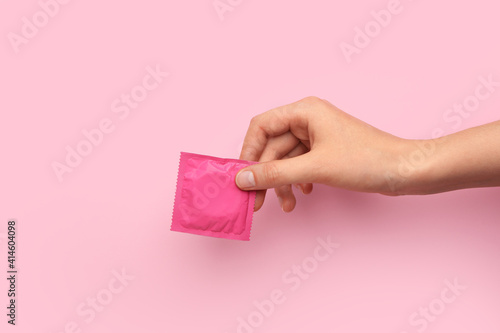 Tableau sur toile Female hand with wrapped condom on color background