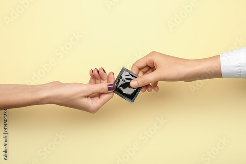 Female hands with wrapped condom on color background