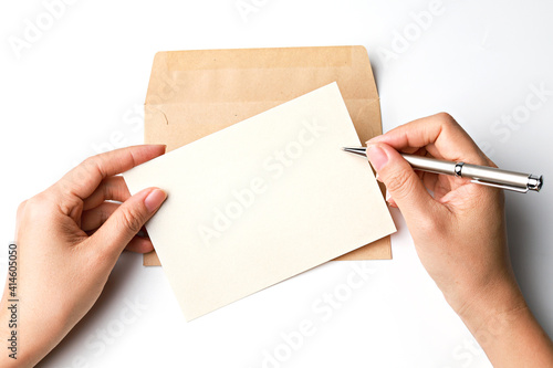 Woman’s hands writing with pen over blank paper card and envelope isolated on white background. Top view