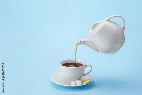 Pouring of hot tea from teapot into cup on color background