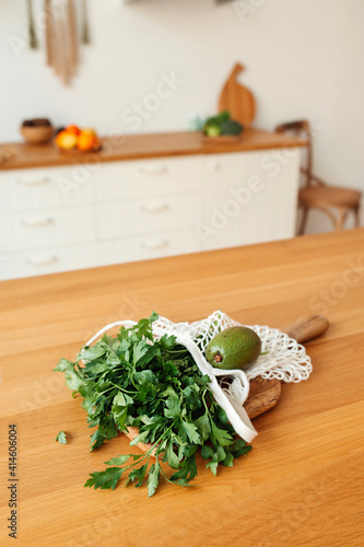 fresh parsley,coriander and avocado in white wicker string bag on wooden table in light Scandinavian-style kitchen. vertical content