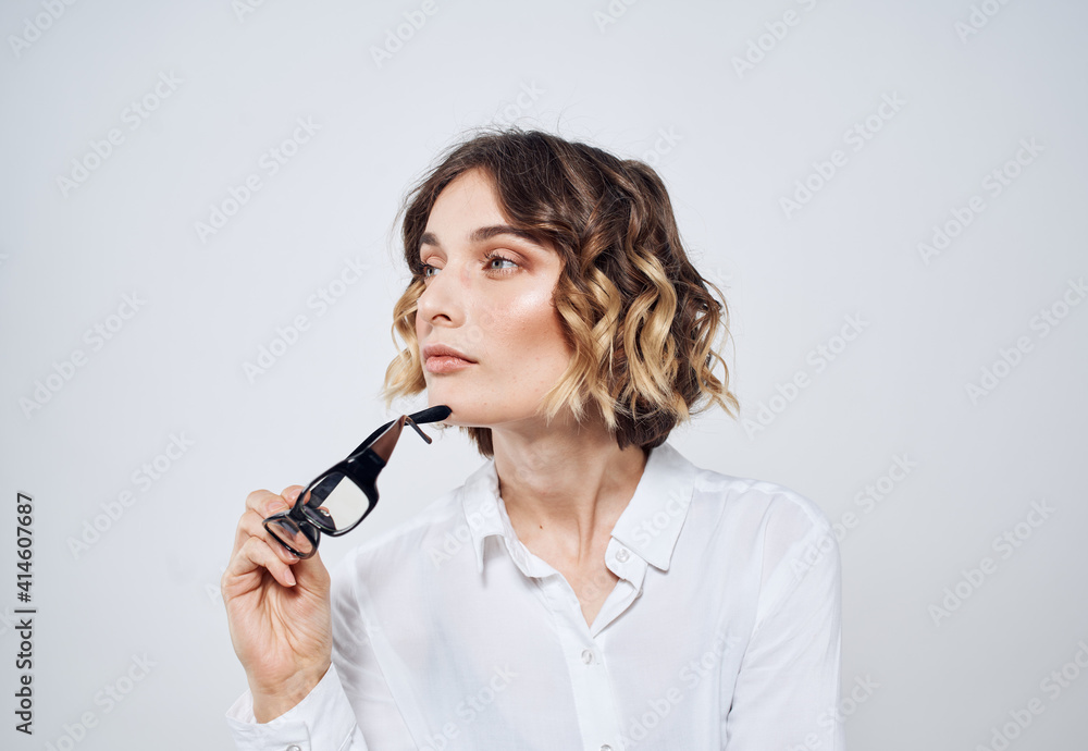 A woman on a light background holds glasses in her hands and a white shirt A woman on a light background holds glasses in her hands and a white shirt