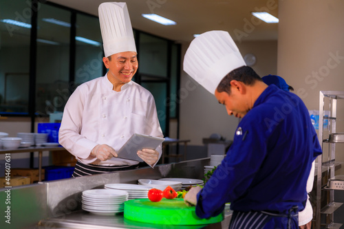 An Asian male chef hold tablet control his team while foods preparation in the kitchen.