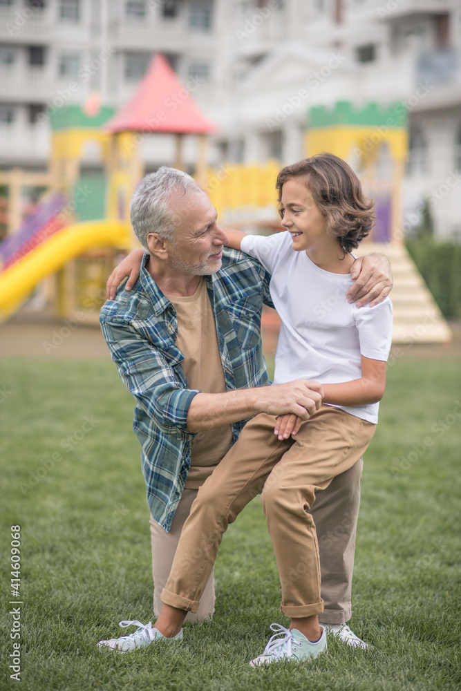 Gray-haired man hugging his son and looking happy Gray-haired man hugging his son and looking happy
