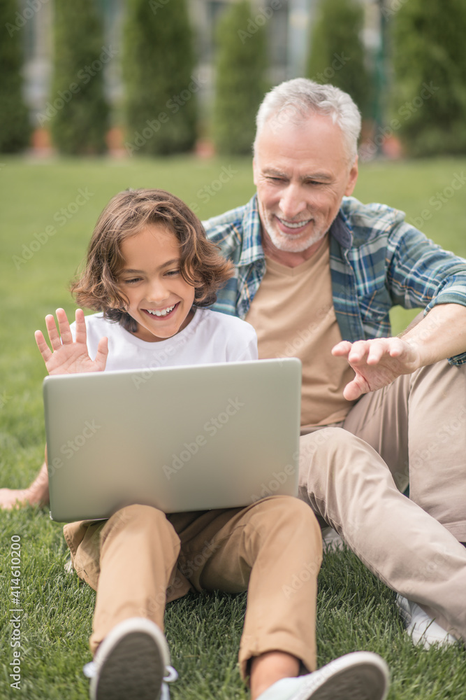 Son and dad sitting together with a laptop and having a video call Son and dad sitting together with a laptop and having a video call