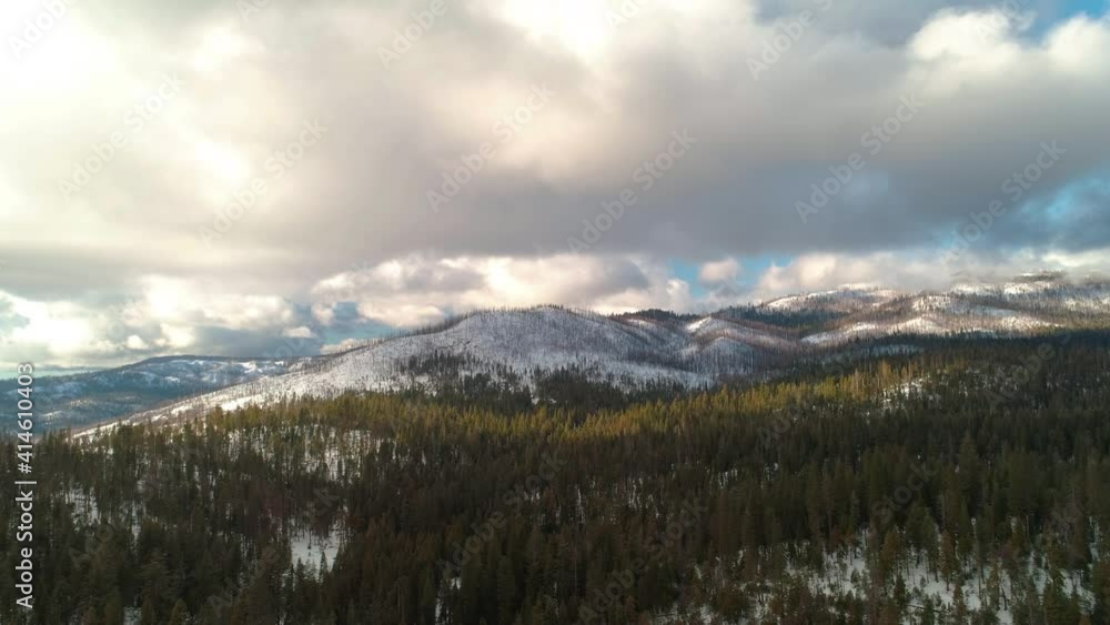 Sideways aerial over epic winter landscape. Snowy mountains and beautiful clouds above. Lush green trees and white snow. Sideways aerial over epic winter landscape. Snowy mountains and beautiful clouds above. Lush green trees and white snow.
