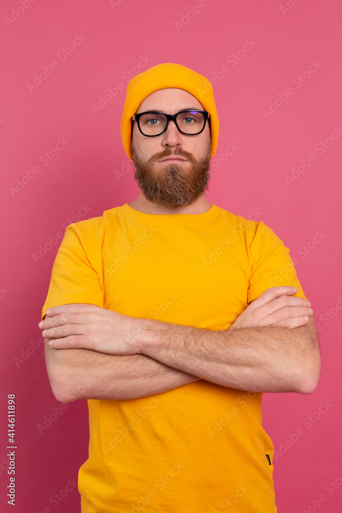 Portrait of stylish handsome european bearded man in casual yellow shirt hat and glasses on pink background Portrait of stylish handsome european bearded man in casual yellow shirt hat and glasses on pink background