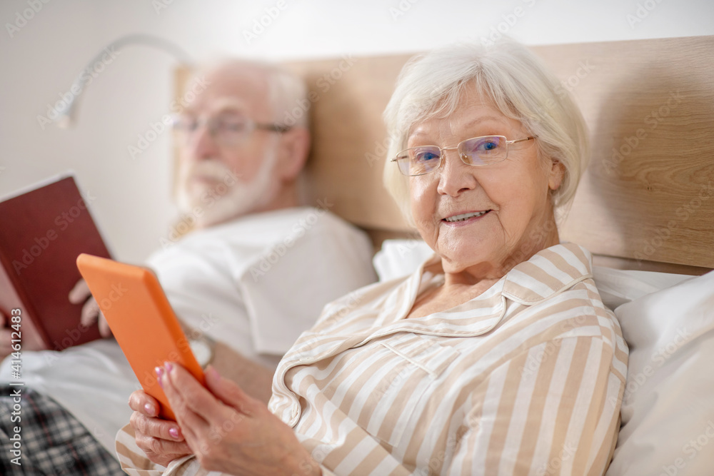 Aged married couple lying in bed and reading and feeling good Aged married couple lying in bed and reading and feeling good