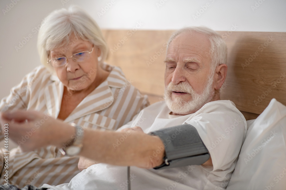 Grey-haired elderly man checking his blood pressure and looking concentrated