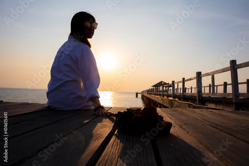 Portrait young woman with bunch red rose sit waiting boy friend at wooden bridge, alone woman sit on bride see outside to see sunset