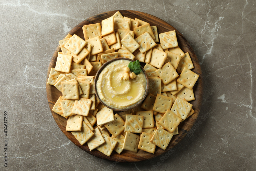 Tray with crackers and bowl of hummus on gray background