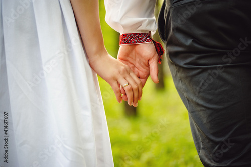 Look at the hands of two lovers who are holding each other. Close-up. Wrist. cropped image. Girl in white dress and man in shirt. Walk around the park.