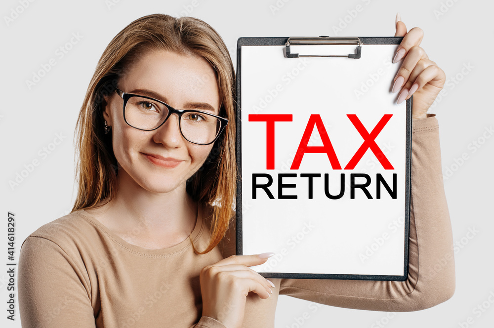 Tax return. Beautiful young business woman wearing glasses holds a clipboard with mock up space isolated on gray background Tax return. Beautiful young business woman wearing glasses holds a clipboard with mock up space isolated on gray background