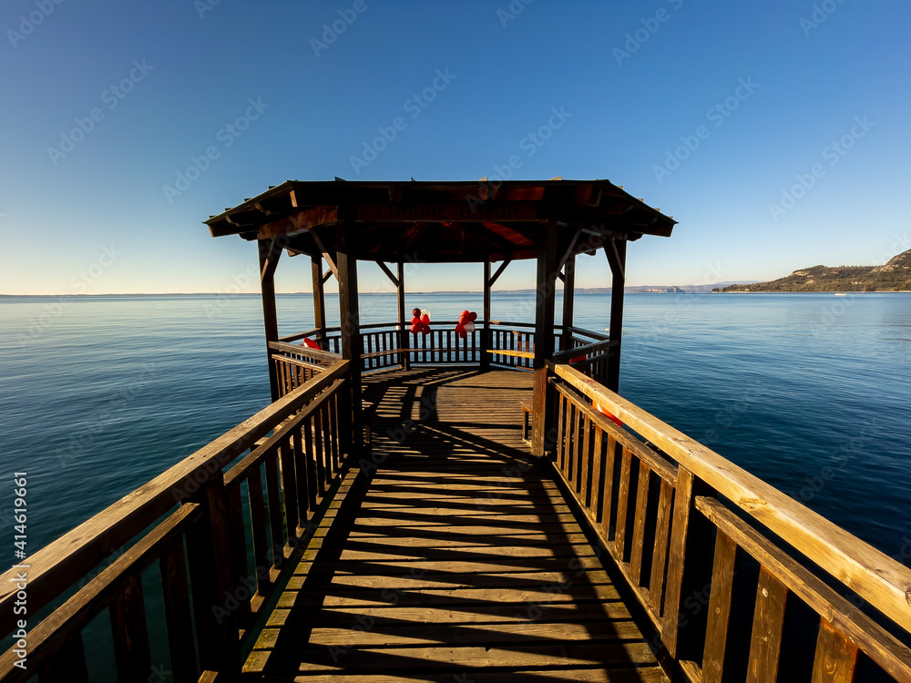 Pleasant view of the coast of Lake Garda. Lonely Sailboat in the middle of the lake on a Sunny day.