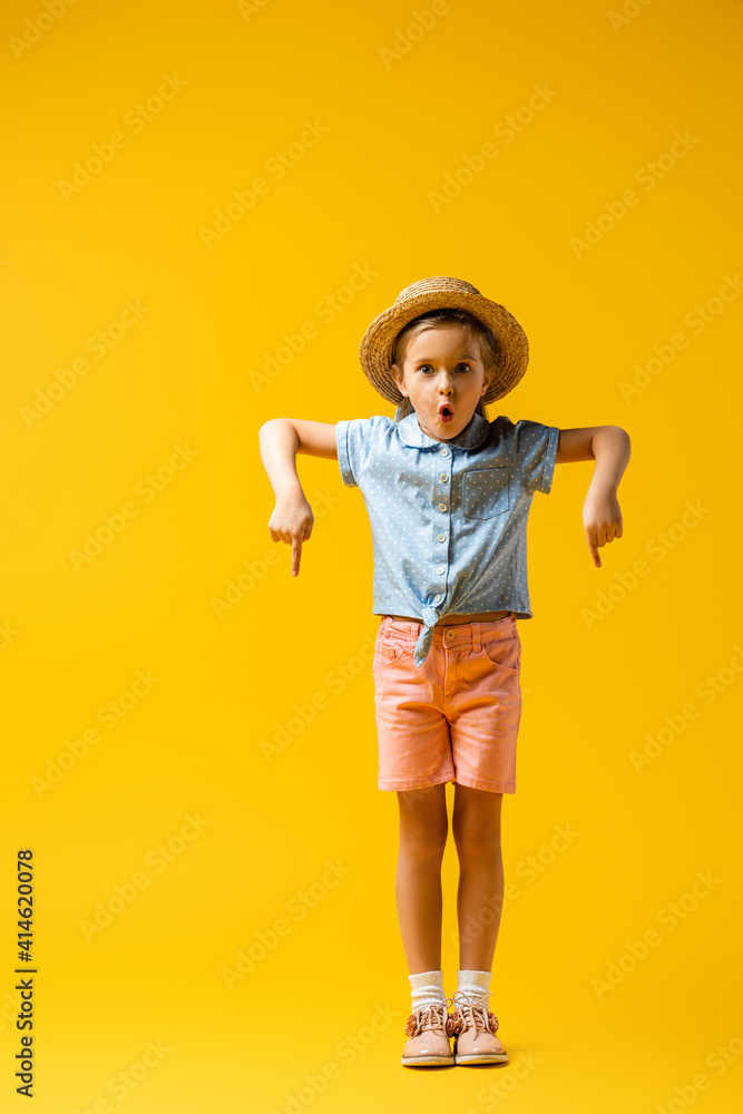 full length of shocked kid in straw hat pointing down with fingers on yellow full length of shocked kid in straw hat pointing down with fingers on yellow