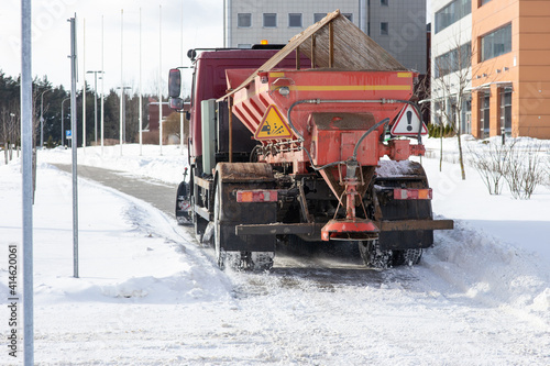 A large orange snowplow cleans snow from the pavement.