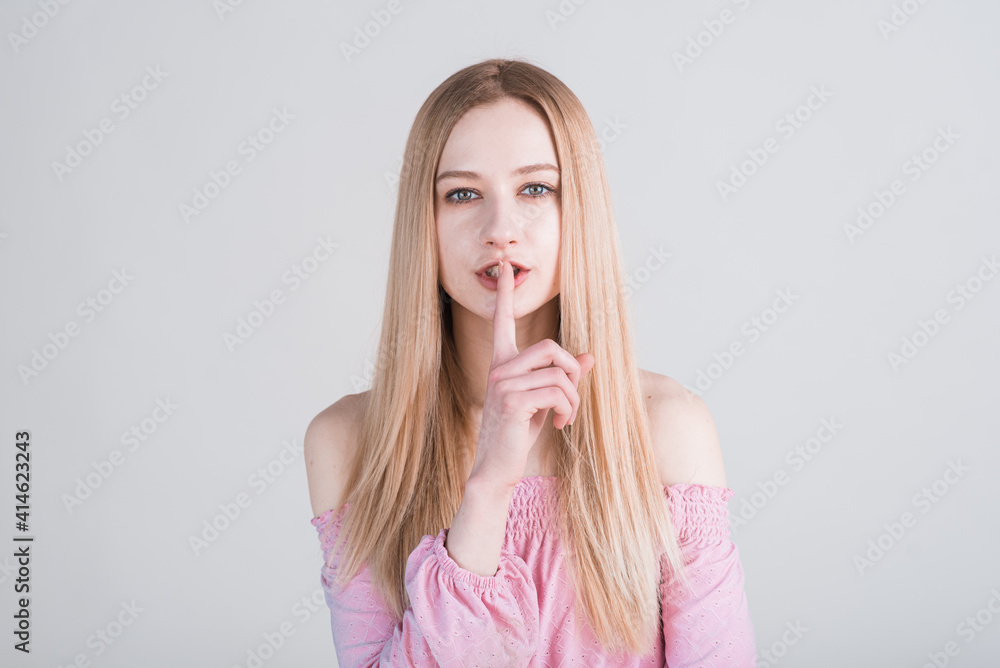 Portrait of a young blonde who holds her finger to her mouth in the studio on a white background. Secret! Portrait of a young blonde who holds her finger to her mouth in the studio on a white background. Secret!