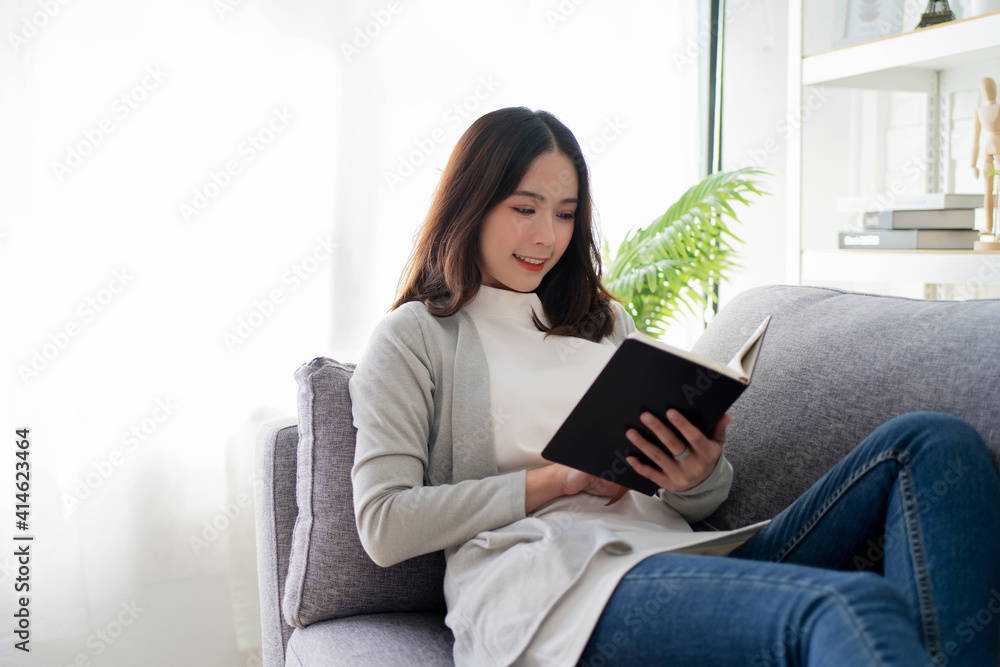 Beautiful young Asian woman reading on a sofa near the window larger. Beautiful young Asian woman reading on a sofa near the window larger.