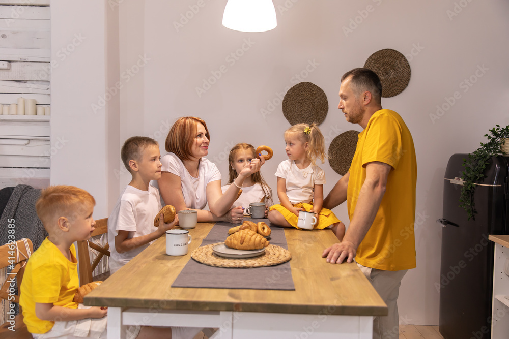 a big family has breakfast together. parents and children in the kitchen. family eats croissants