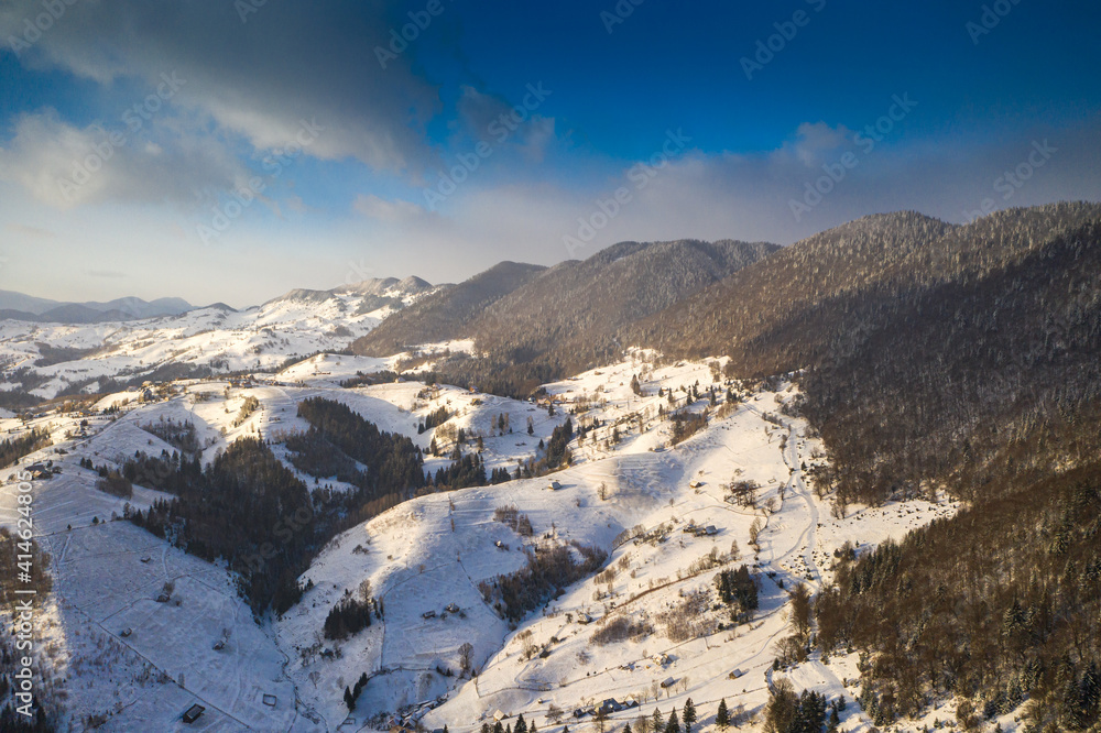 Aerial scenic rural view over Pestera village at the bottom of Piatra-Craiului Mountains during a freezing winter in Romania with authentic houses