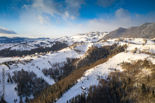 Aerial scenic rural view over Pestera village at the bottom of Piatra-Craiului Mountains during a freezing winter in Romania with authentic houses