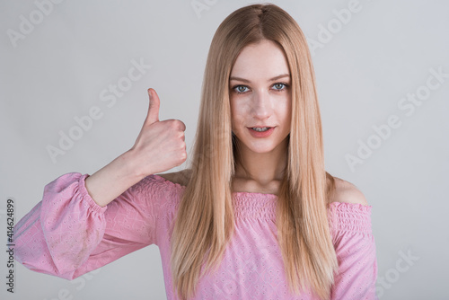 Portrait of a blonde girl who shows thumbs up in the studio on a white background
