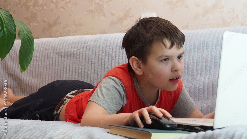 boy using a laptop for playing online games and wearing headphone at home, a boy at a computer or tablet at home on the couch, communicating with friends, blogging, studying online boy using a laptop for playing online games and wearing headphone at home, a boy at a computer or tablet at home on the couch, communicating with friends, blogging, studying online