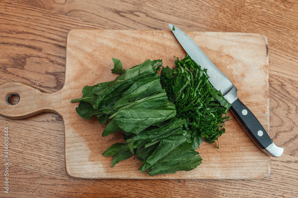 Cut sorrel leaves and a knife on a wooden board. Chopped greens for cooking Cut sorrel leaves and a knife on a wooden board. Chopped greens for cooking