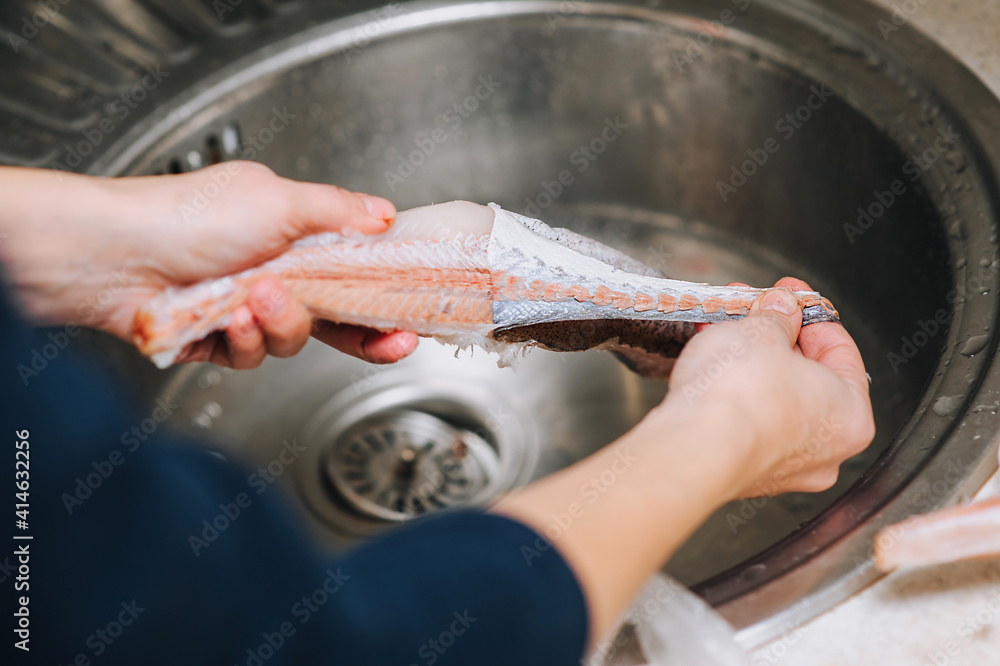 The girl cook in the washstand with her hands cleans the raw sea, river fish hake from the skin for cooking.