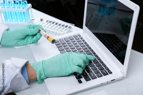 doctor holds blood test tube and typing on laptop. entering blood test results into the database