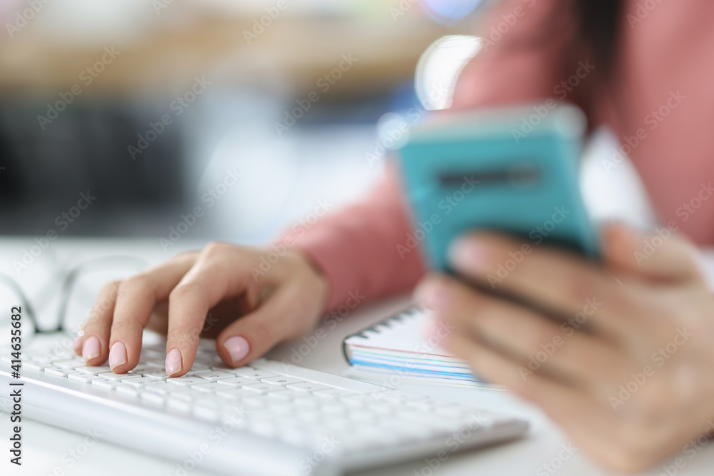 In female hand a smartphone and second hand on computer keyboard In female hand a smartphone and second hand on computer keyboard