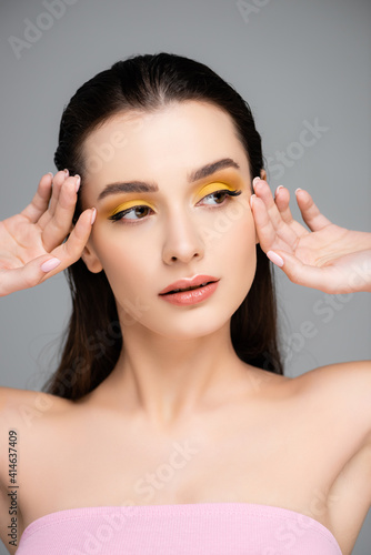 brunette young woman with yellow eyeshadow looking away isolated on grey