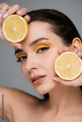 young brunette woman holding yellow lemon halves isolated on grey
