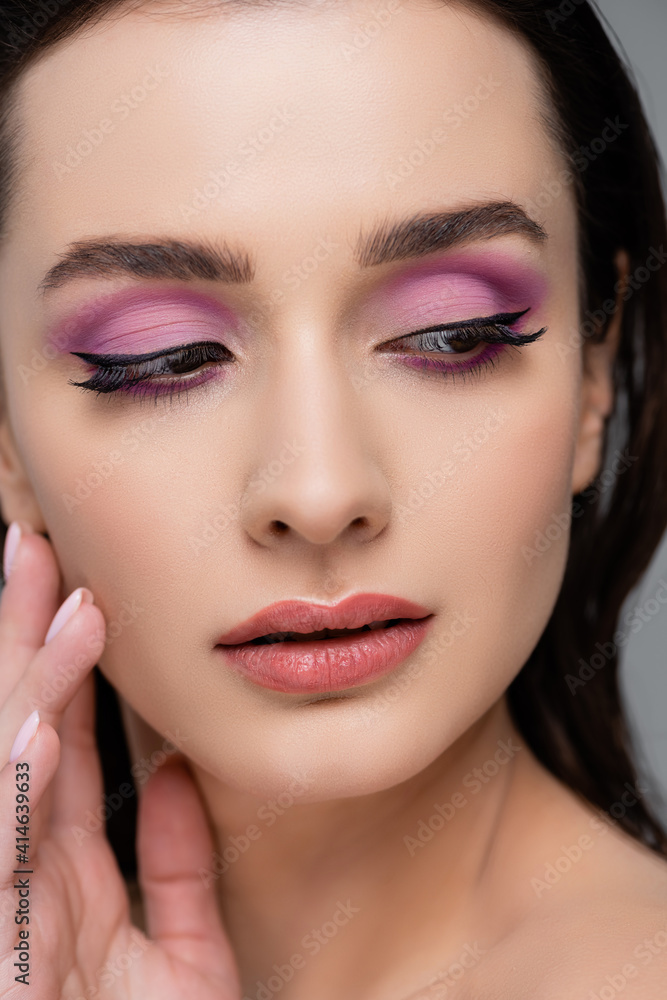 close up of brunette woman with pink eye shadows looking away isolated on grey