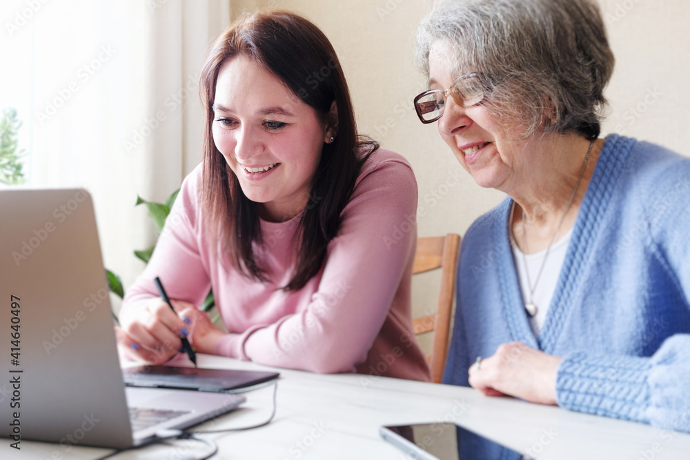 Girl designer carries out a project ordered by an elderly woman businessman - Young and elderly woman use a laptop and a graphic tablet - Modern technologies for creating content. Girl designer carries out a project ordered by an elderly woman businessman - Young and elderly woman use a laptop and a graphic tablet - Modern technologies for creating content.