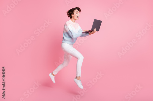 Full length photo portrait of excited girl with laptop jumping up isolated on pastel pink colored background © deagreez