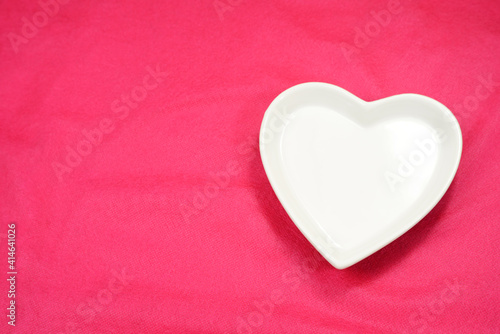 White heart, heart shaped plate-dish, light color heart-shaped plate. Dishes for food, for dinners, weddings or romantic moments. Pink background. Dinner ideas. Sign of romantic.   