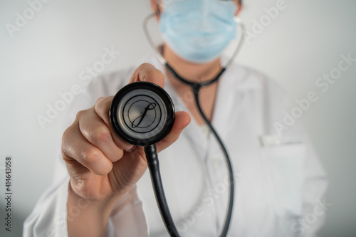 Doctor with mask with phonendoscope to listen to heart of patient.