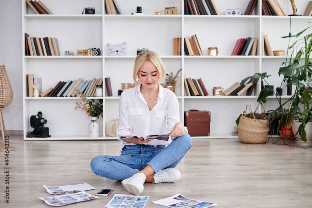 Young blond woman, wearing casual jeans and white top, sitting on floor, reading magazine. Freelancer employed at home. Work process in modern company office. Young successful professionals. Young blond woman, wearing casual jeans and white top, sitting on floor, reading magazine. Freelancer employed at home. Work process in modern company office. Young successful professionals.